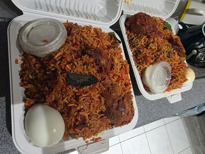 Takeout boxes of chicken biryani with a boiled egg and raita