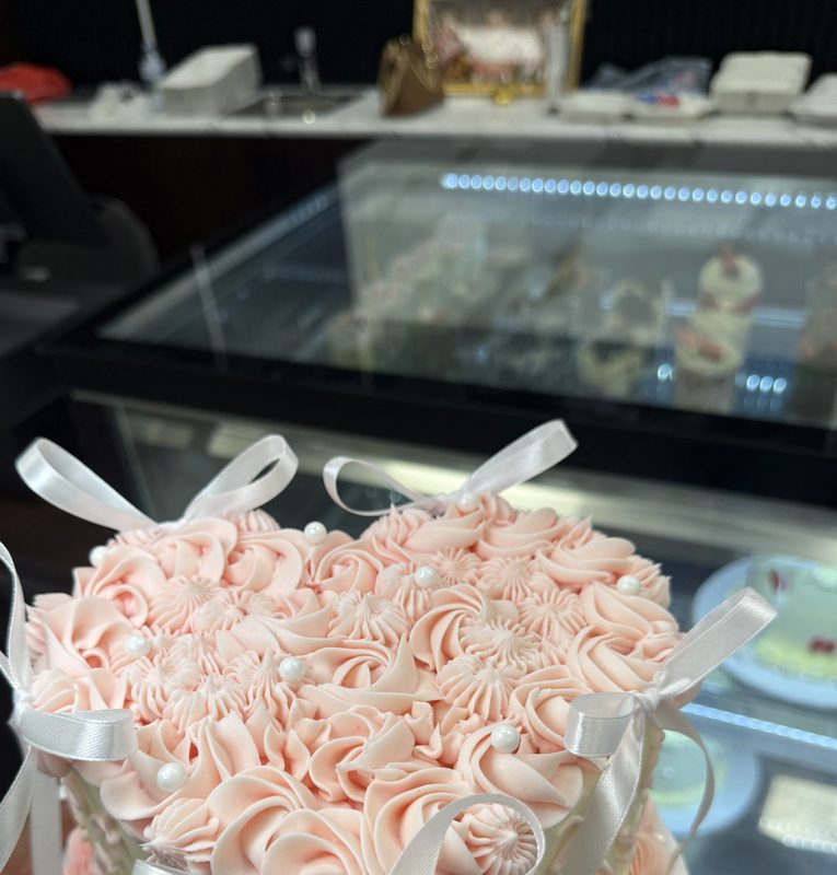 A blush pink rosette cake with white ribbon